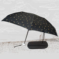 A black DrizzlePro umbrella with small gold musical note patterns is open next to its black zippered case on a sketched
