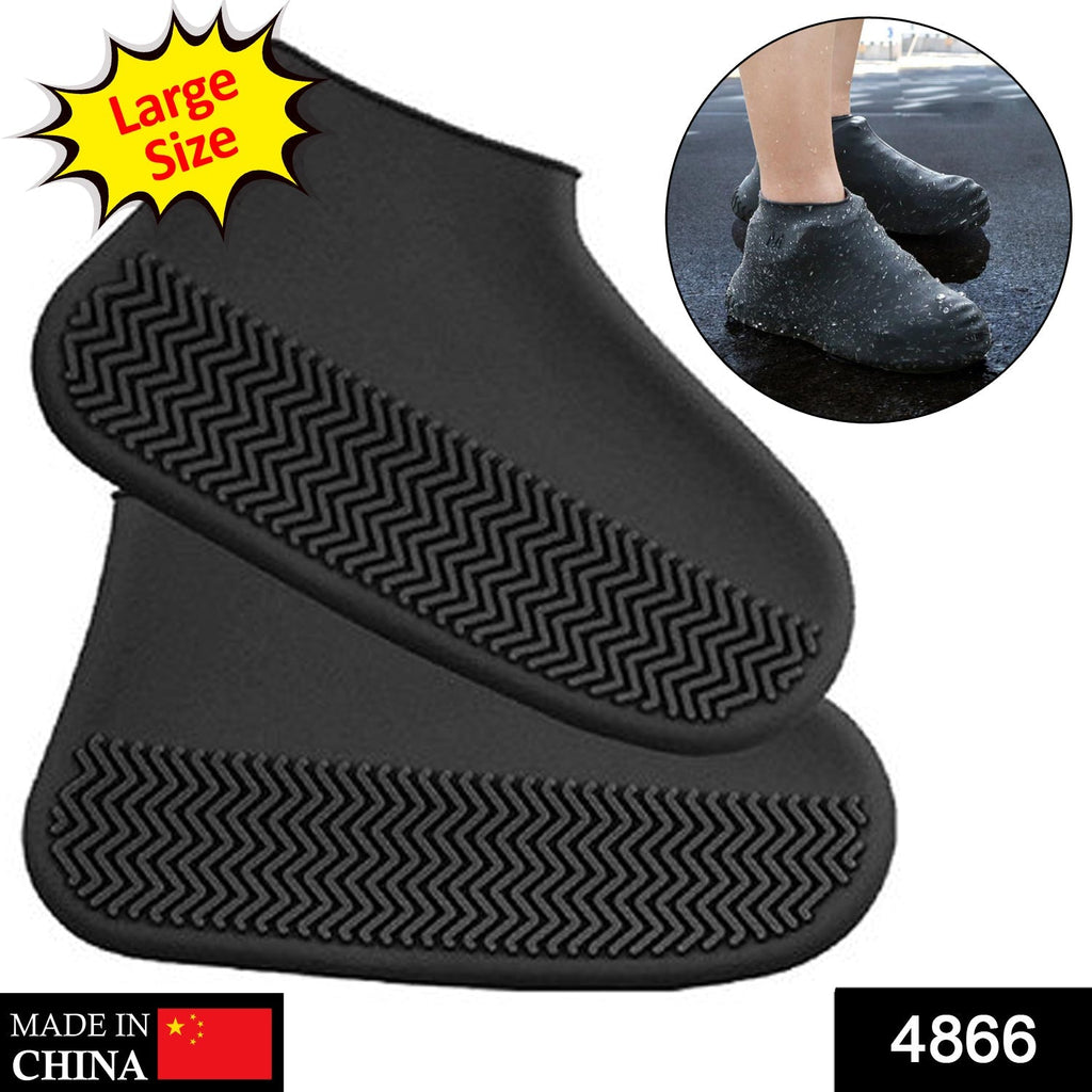 A person's feet wearing black silicone shoe covers stand on a wet wooden deck.